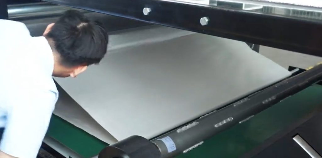 The operator inspects the fabric surface and fabric feed after the sublimation transfer process.